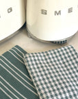 Two green kitchen towels on a countertop with a Smeg appliance in the background.