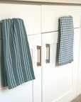 Green and white checkered towels hanging on a kitchen cabinet.