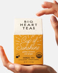 Yellow tea box packaging held by two hands on a white background.