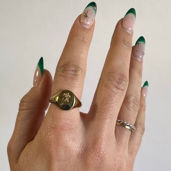 A woman's hand wearing a gold plated ring with an aquarius zodiac symbol engraved into the ring. She is wearing the ring on her right pointer finger
