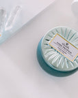 Voluspa Casa Pacific Baby Blue Candle next to book corner with two crystals.