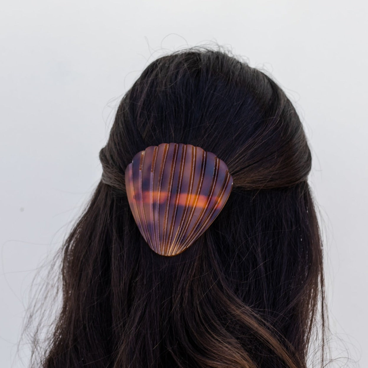 Girl with dark brown hear wearing a brown tortoise seashell hair clip with her hair half up, against a white background