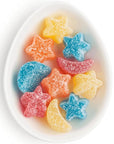 Star and moon shaped sour gummies in varying colors like blue, yellow, orange, and red. Candy's are in an oval white dish