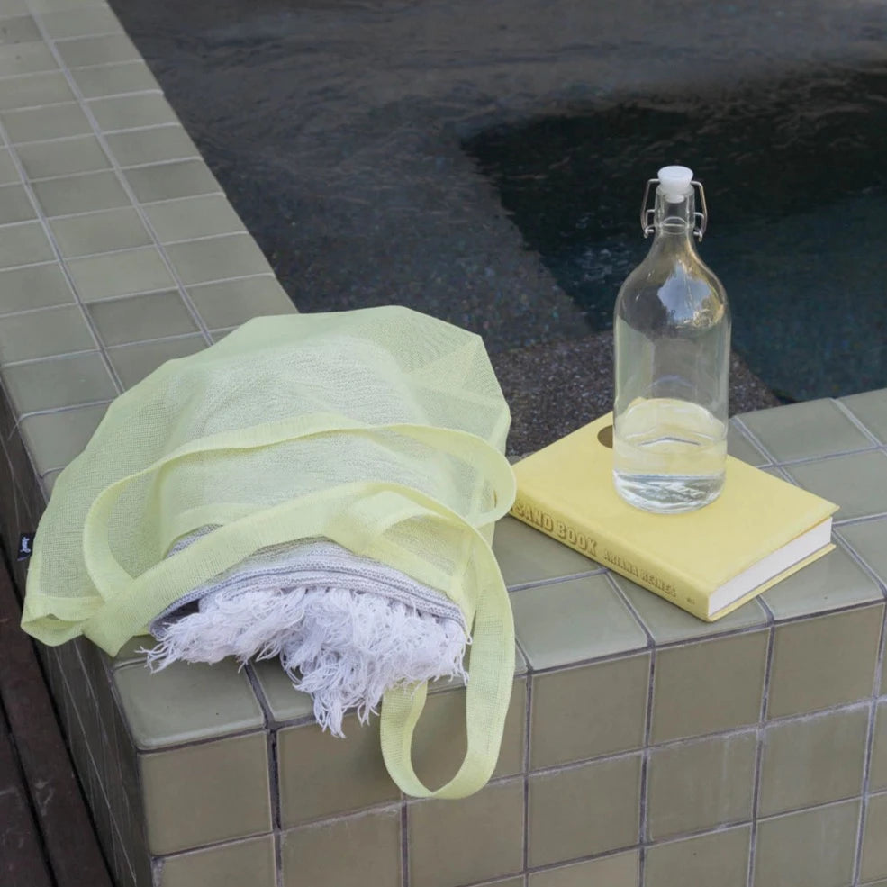 yellow market tote with towel in it resting on a brown ceramic flower edge with yellow book and clear glass bottle next to it