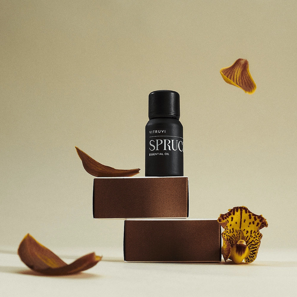 Vitruvi Spruce essential oil bottle on a beige background with decorative elements.