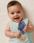 Baby holding a blue checkered bow tie and teddy bear toy against a beige background