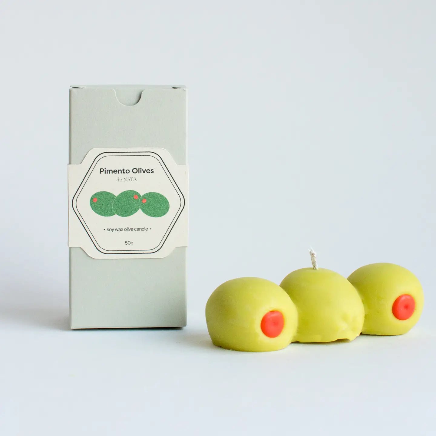 Candle shaped like pimento olives with a box labeled 'Pimento Olives' on a light gray background