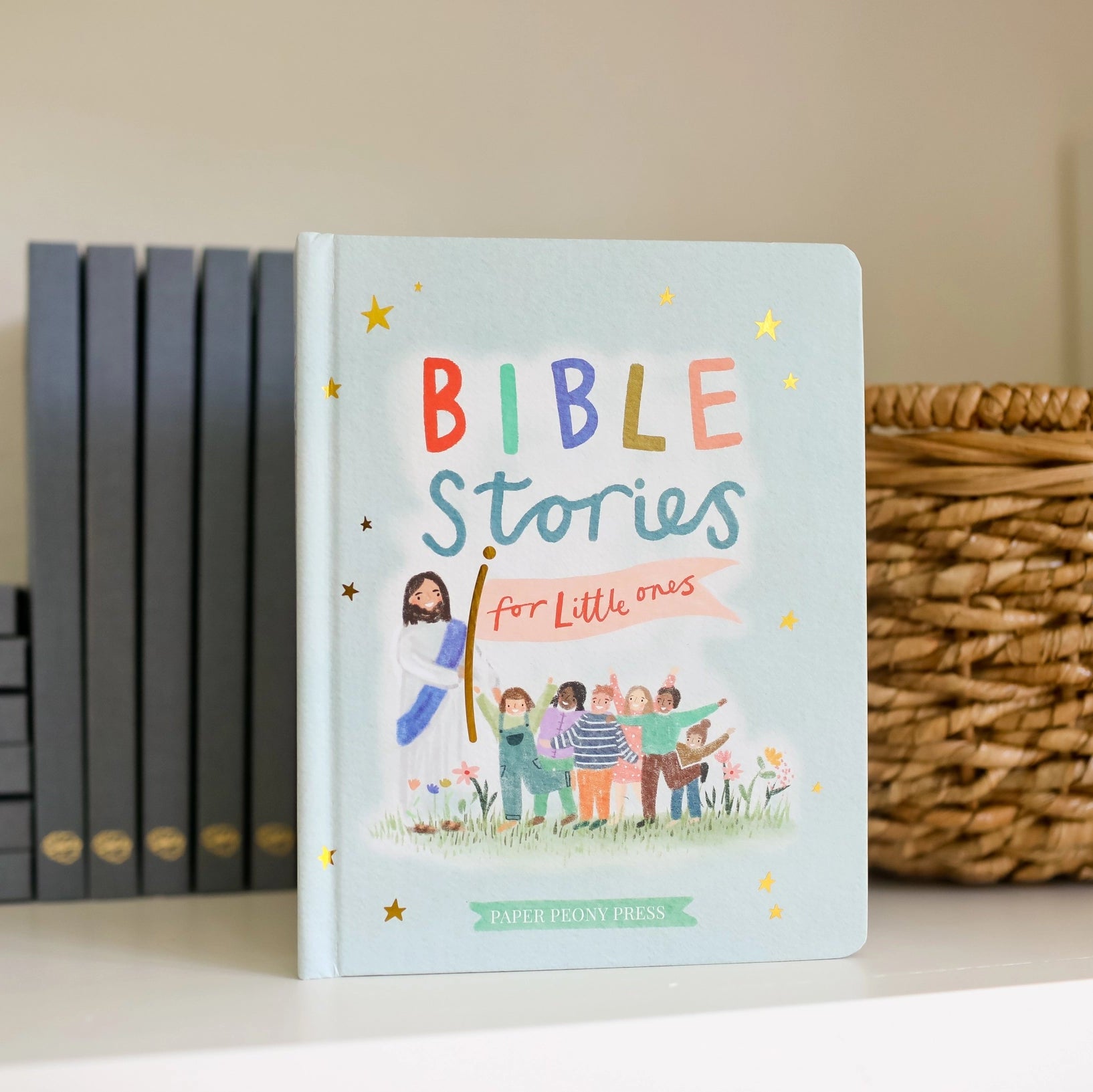 Children's book titled 'Bible Stories for Little Ones' on a shelf with other books and a basket.