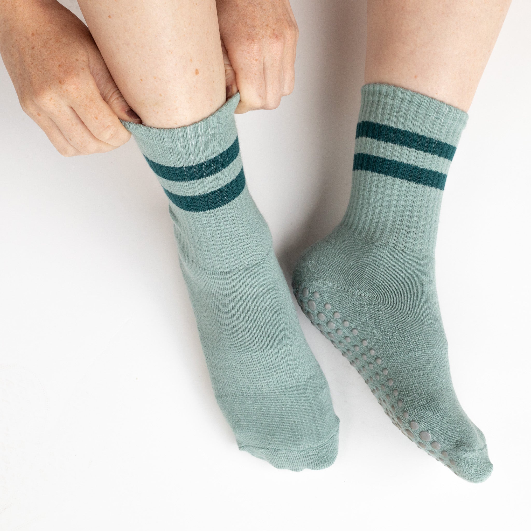A woman wearing Blue & Teal Grippy Socks while sitting on a white background.