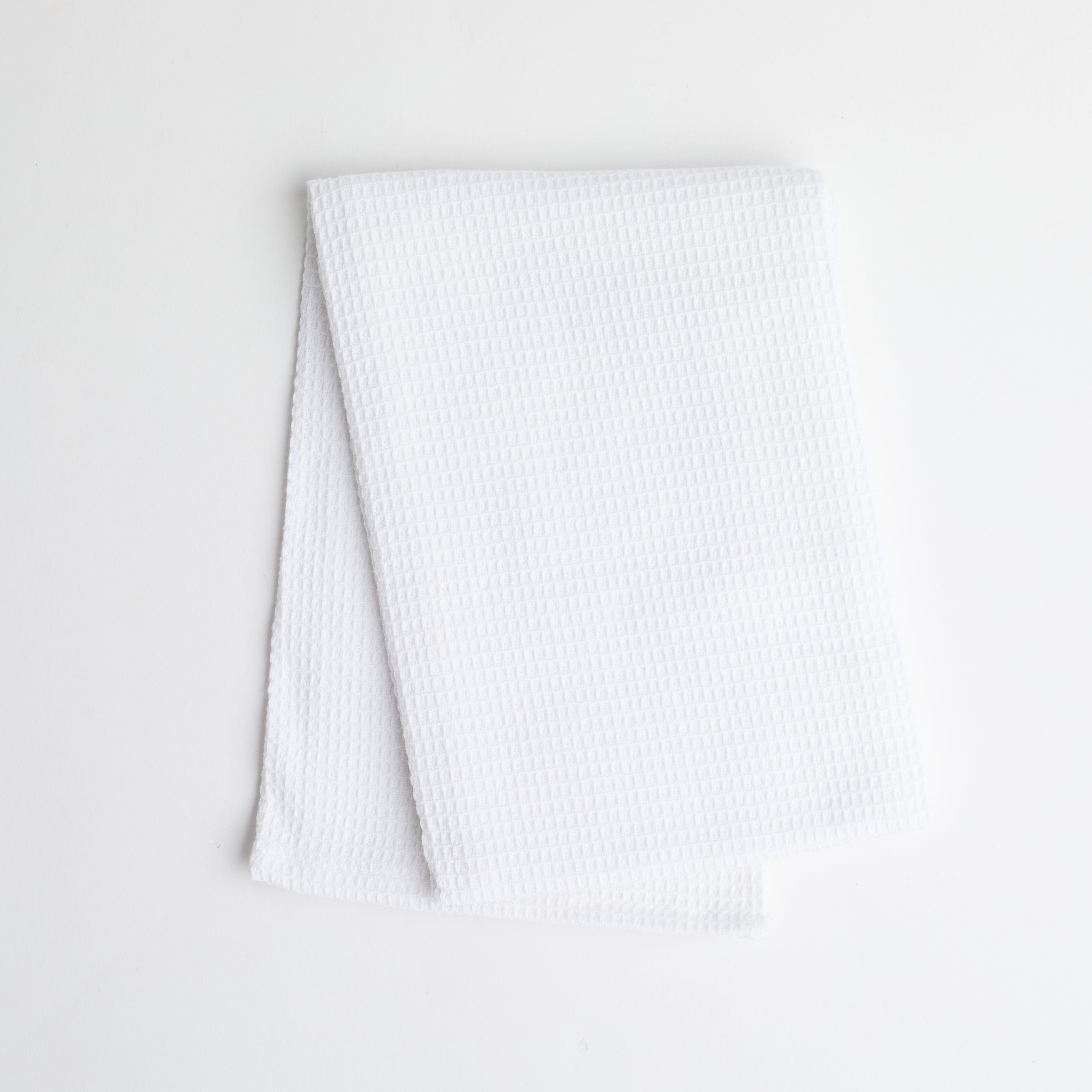 A white colored waffle knit dish towel folded on a white background