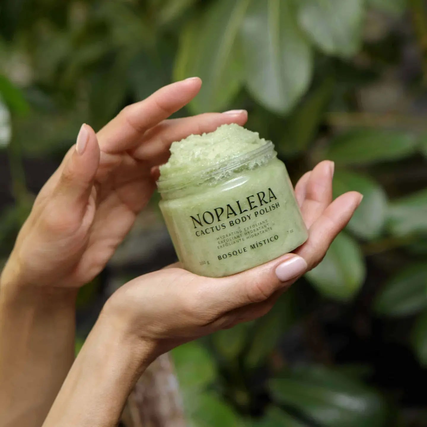 Hand holding a jar of Nopalera Cactus Body Polish against a green leafy background