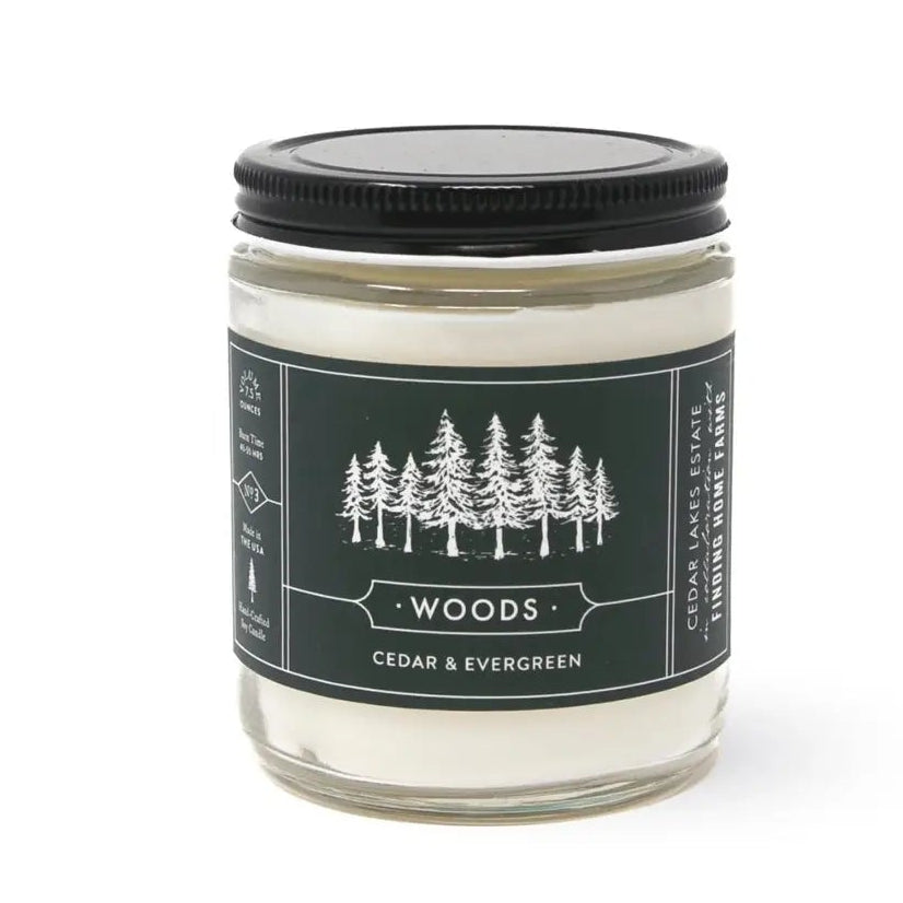 Candle jar labeled 'Woods' with a black lid on a white background