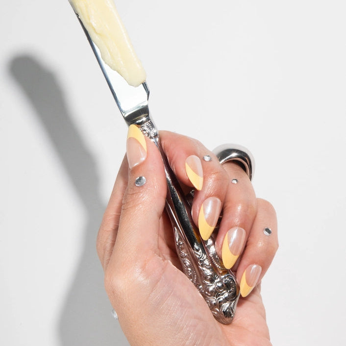 Hand holding a silver and cream-colored tool against a light gray background