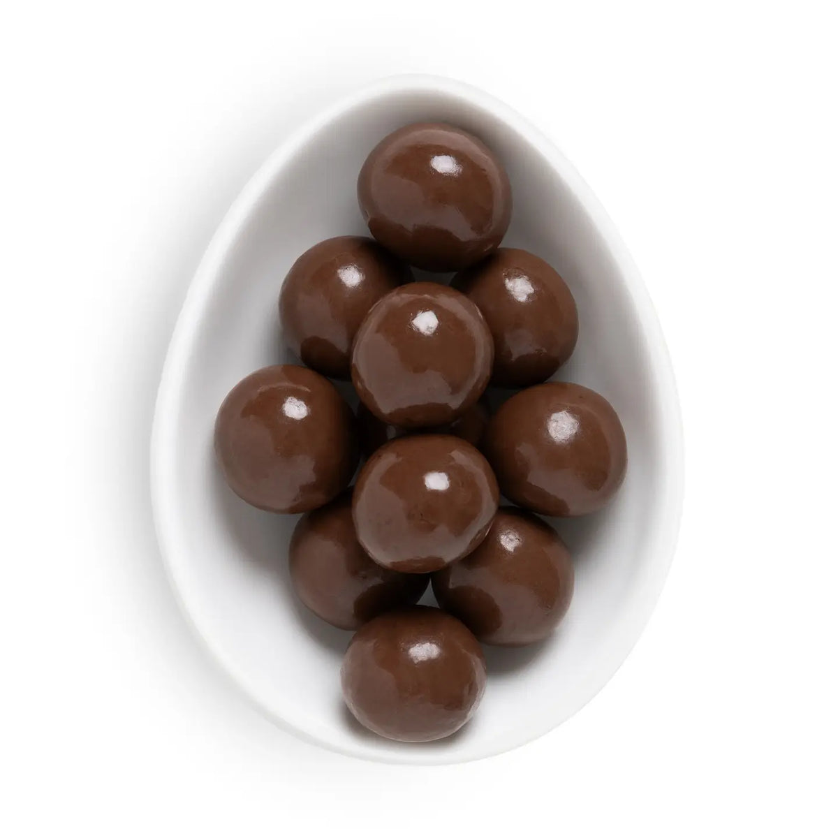 A top-down view of glossy brown chocolate-covered round candies piled in a white egg-shaped dish on a white background.