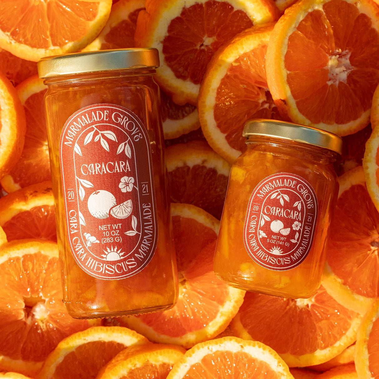 Two jars of marmalade with a visible brand label on a background of sliced oranges.