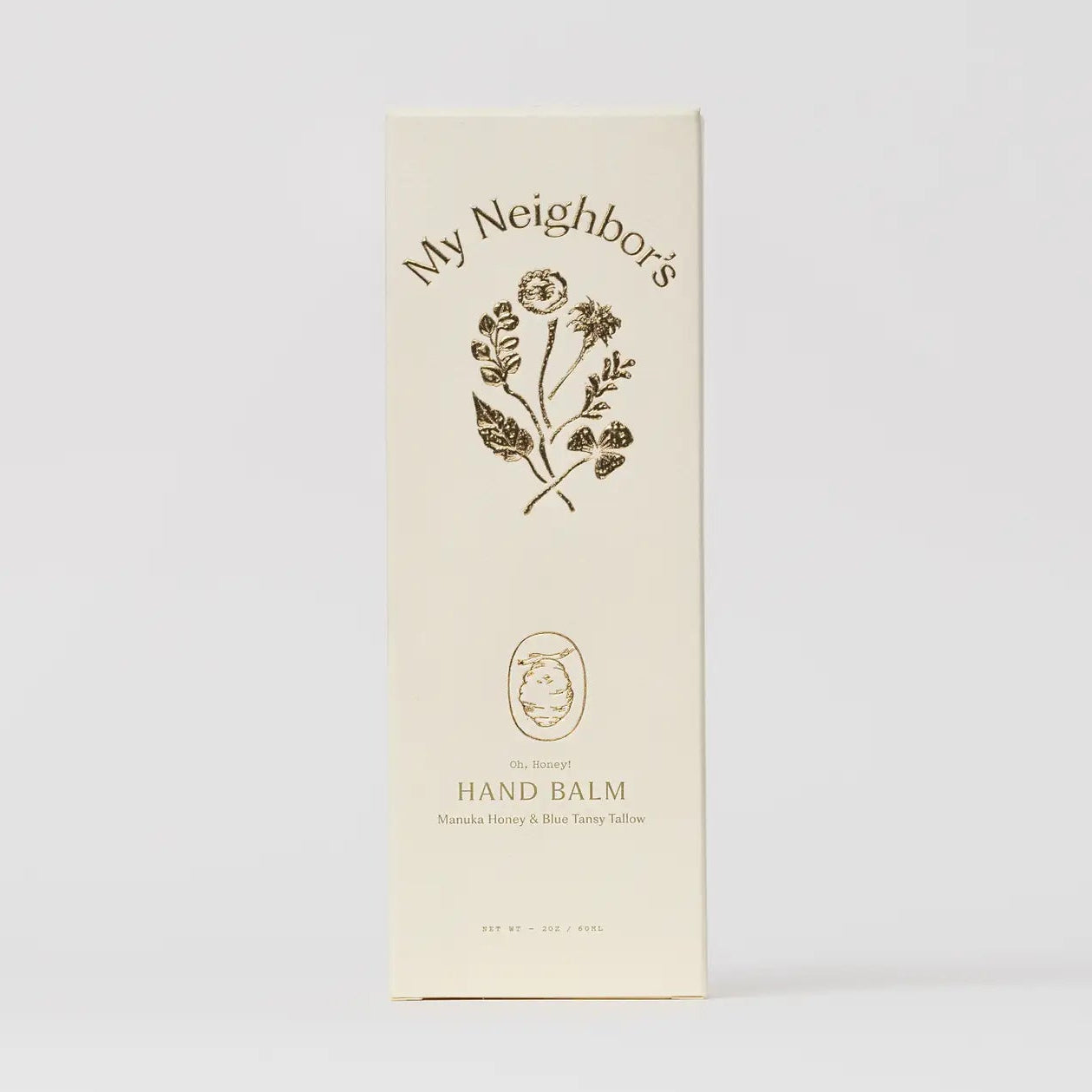A tall cream-colored product box for 'My Neighbor's Hand Balm' featuring a dark brown botanical illustration and text, set against a clean, light gray background.