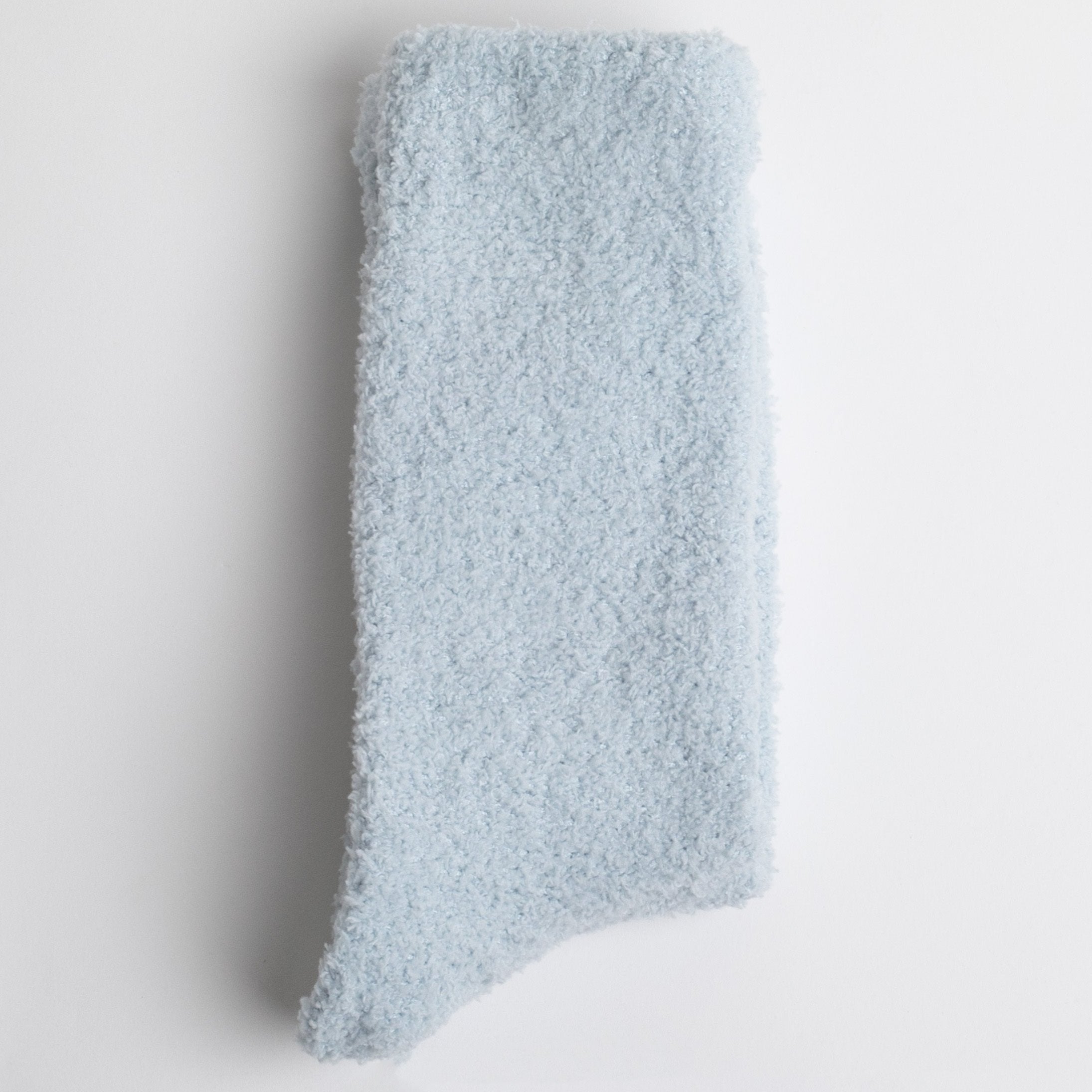 folded light blue fuzzy socks. material is fluffy and cozy, suggesting it could provide warmth or comfort. It is laid flat against a plain white background.






