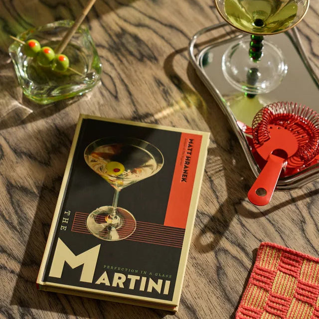 Cocktail setup with a Martini book, glasses, and bottles on a wooden surface.