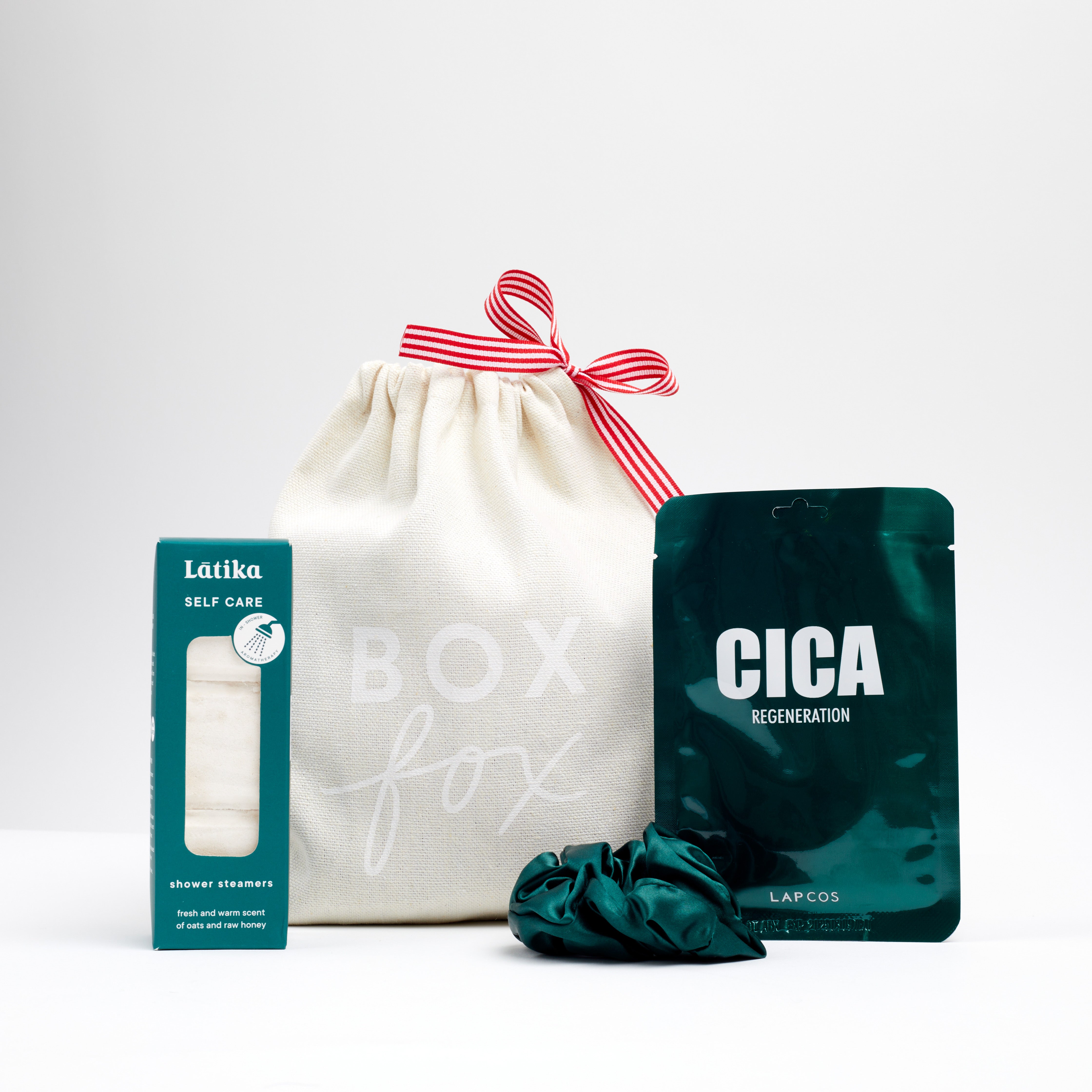 White stocking stuffer bag with red and white ribbon with Latika self care shower steamers. azeria green silk scrunchies and Lapcos Cica Face Mask 