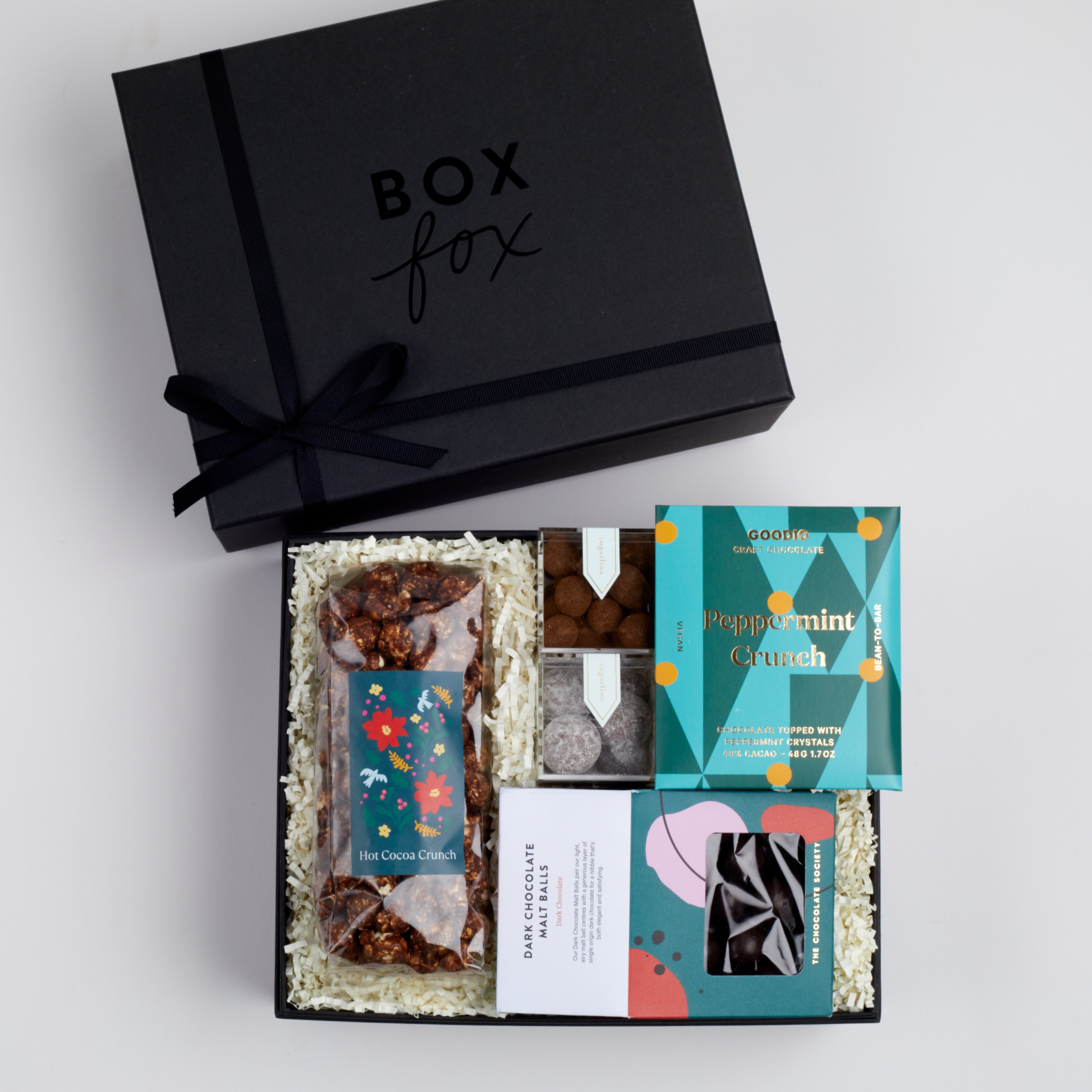 BOXFOX black gift box packed with hot cocoa crunch popcorn, dark chocolate malt balls, sugarfina candies and goodio peppermint crunch chocolate
