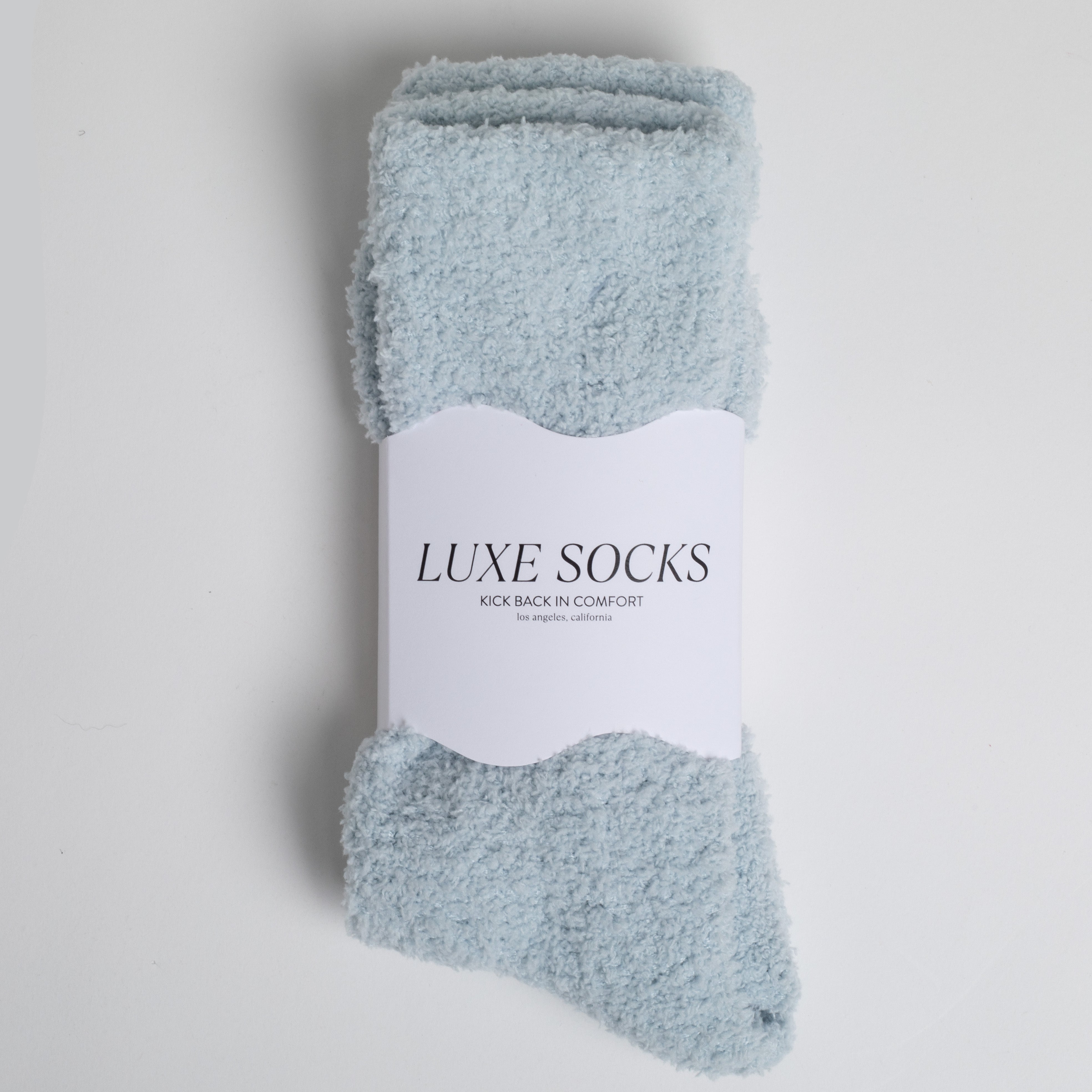 light blue fuzzy socks wrapped in band that says 'LUXE SOCKS'