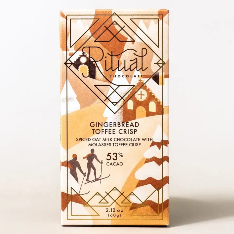 The image shows a product from Ritual Chocolate, specifically the "Gingerbread Toffee Crisp" bar. The packaging is decorated with festive gingerbread house and snow-like patterns in shades of brown and beige. The text on the front of the box reads "Ritual Chocolate" in an elegant script, with the flavor labeled as "Gingerbread Toffee Crisp" below. It is described as "Spiced Oat Milk Chocolate with Molasses Toffee Crisp" and contains 53% cacao. The packaging also indicates a weight of 2.12 oz (60g).  