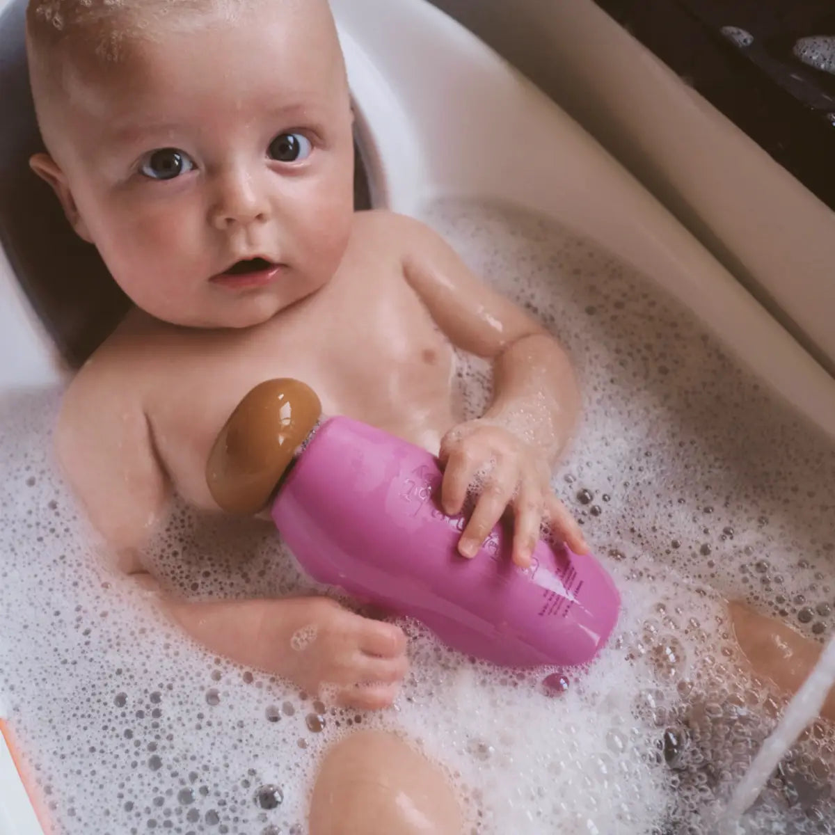 Baby in a bathtub with bubbles holding a purple toy