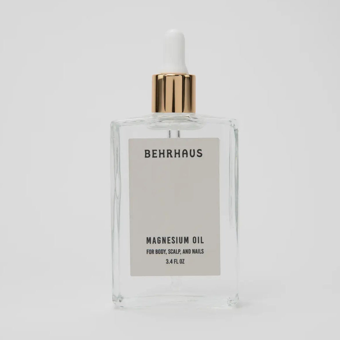 Clear bottle of Behrhaus magnesium oil with a gold cap on a light gray background