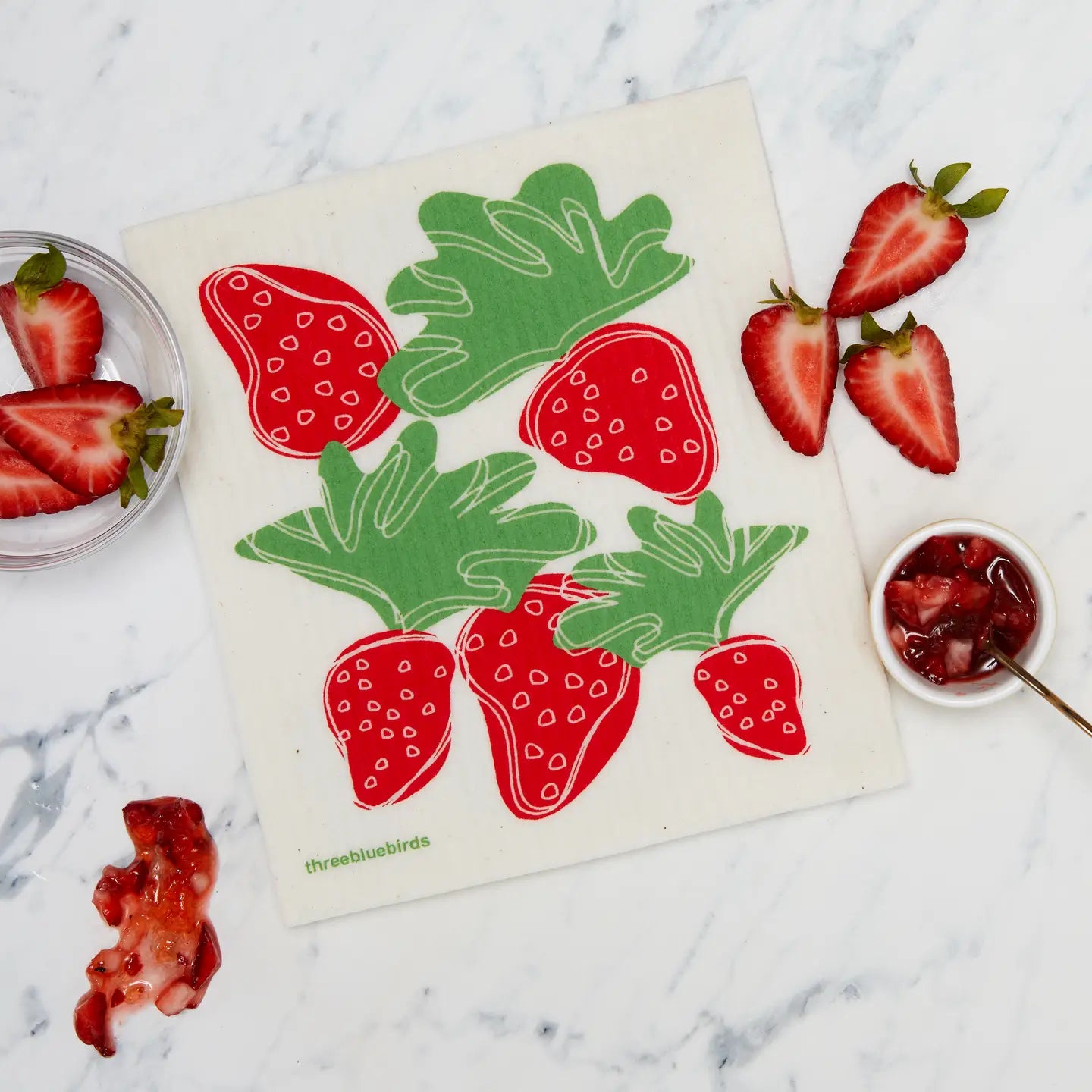 Strawberry-themed kitchen towel on a marble surface with strawberries and jam.
