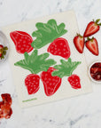 Strawberry-themed kitchen towel on a marble surface with strawberries and jam.