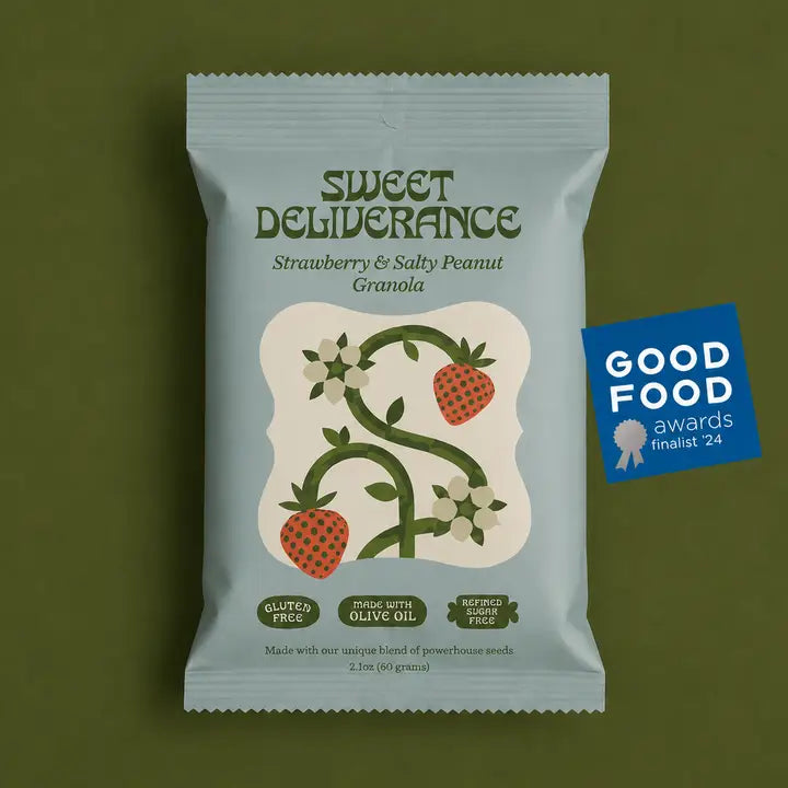 A package of Sweet Deliverance Strawberry &amp; Salty Peanut Granola sits on a solid olive green background. The packaging is a dusty light blue-gray color with dark green text and an illustration of strawberries and vines.