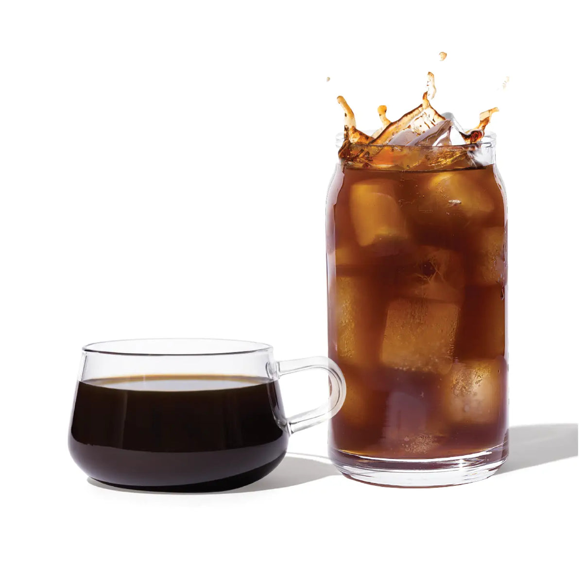 Glass of iced coffee with a splash next to a cup of black coffee on a white background