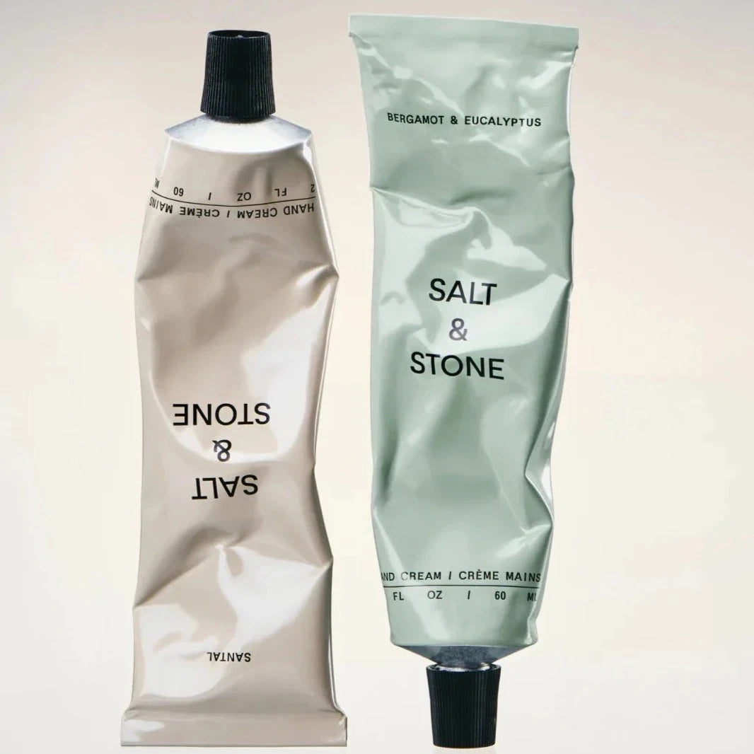 Squeezed tubes of the gray sandal and green bergamot hand lotions placed next to each other