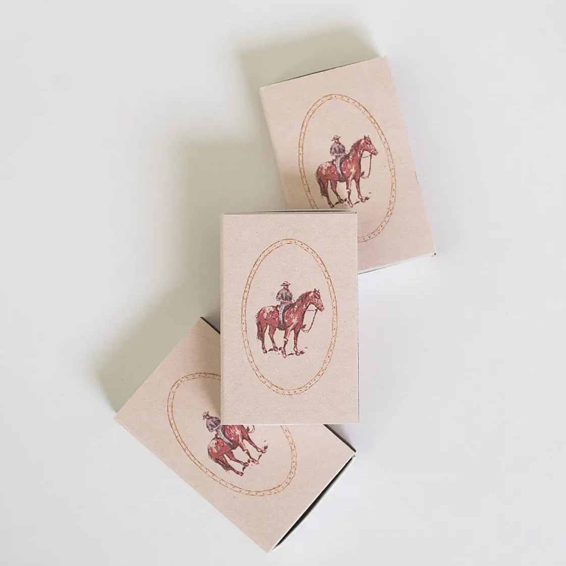 Three beige rectangular boxes arranged diagonally on a white background, each printed with a vintage-style illustration of a rider on a horse inside an oval frame.
