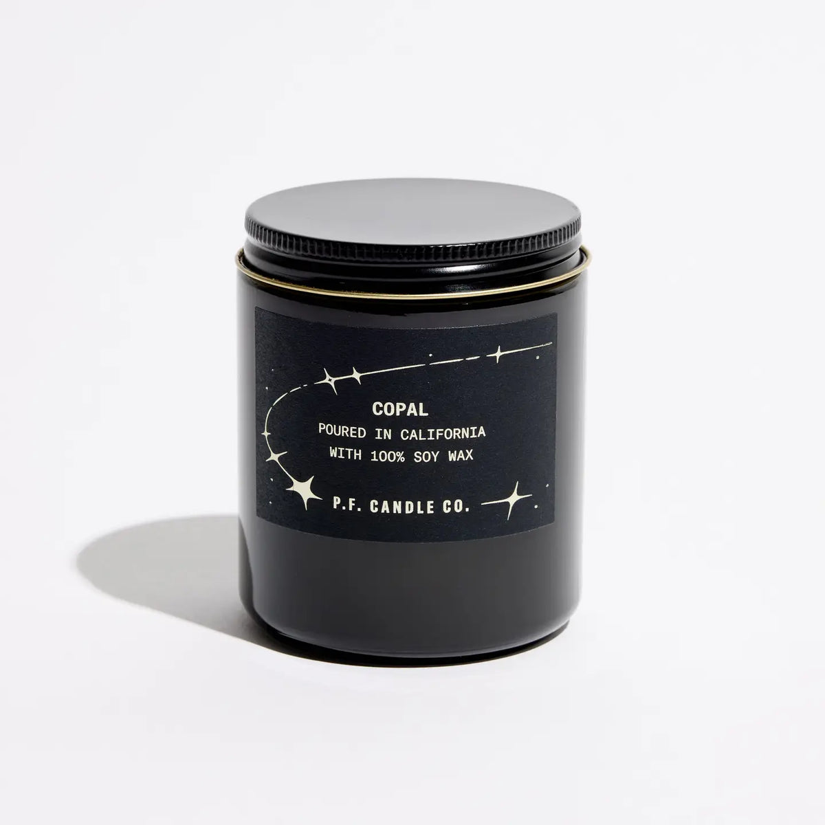 A black glass jar candle with a black lid and a black label featuring white text and star illustrations. The label reads 'COPAL POURED IN CALIFORNIA WITH 100% SOY WAX' and 'P.