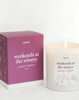 A lit white scented candle next to its magenta and white packaging box, both labeled 'Literie weekends at the winery' with wine-themed line drawings.
