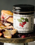 Jar of raspberry jam labeled 'Finding Home' on a plate with pie slices.
