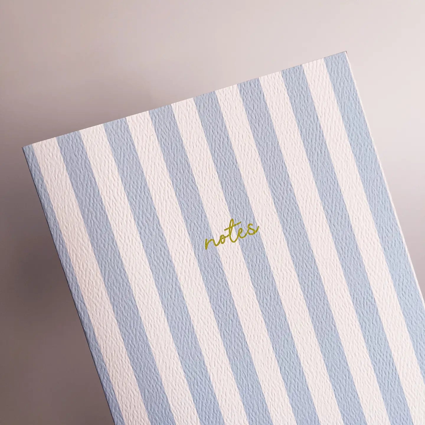 Notebook with blue and white striped cover and 'notes' text on a gray background