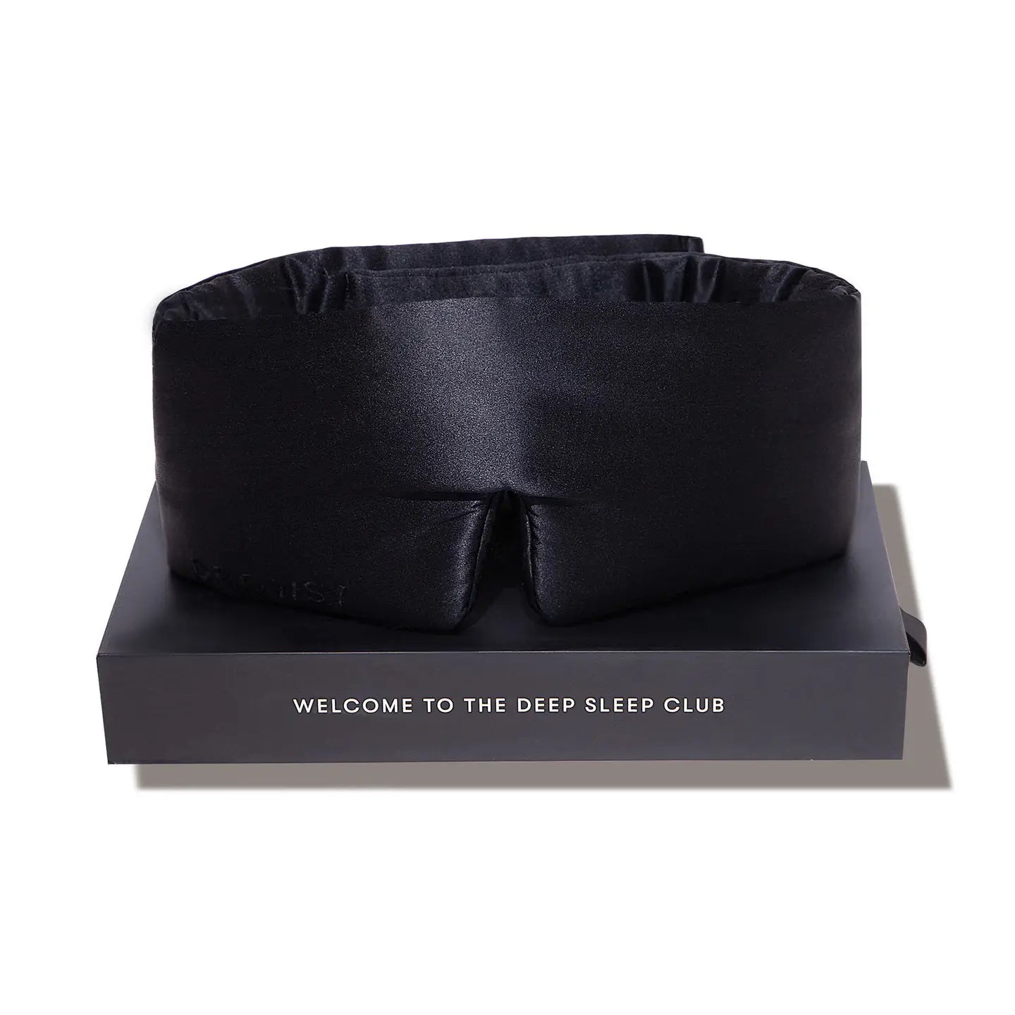 Black satin sleep mask on a black box with 'Welcome to the Deep Sleep Club' text on a white background