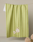 Green striped towel with teapot and cup design hanging on a line against a beige wall.