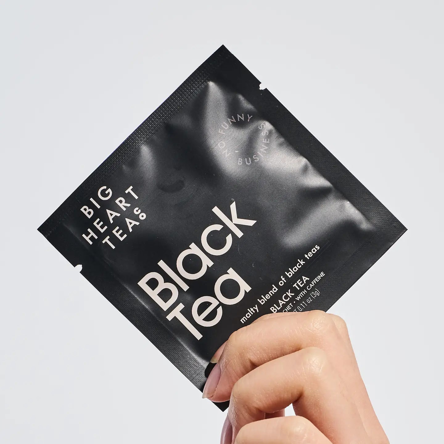 Black tea package held by a hand on a light gray background