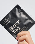 Black tea package held by a hand on a light gray background