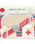 This image shows an "Après Ski Set" by Pinch Provisions, a packaged set labeled as containing six essentials. The visible items include a sleep mask, a mini "Shotski," a collapsible shot glass, a scrunchie, and a hangover kit. The packaging is transparent with a silver zipper, and the background features a cozy, wintery theme with red and cream tones.
