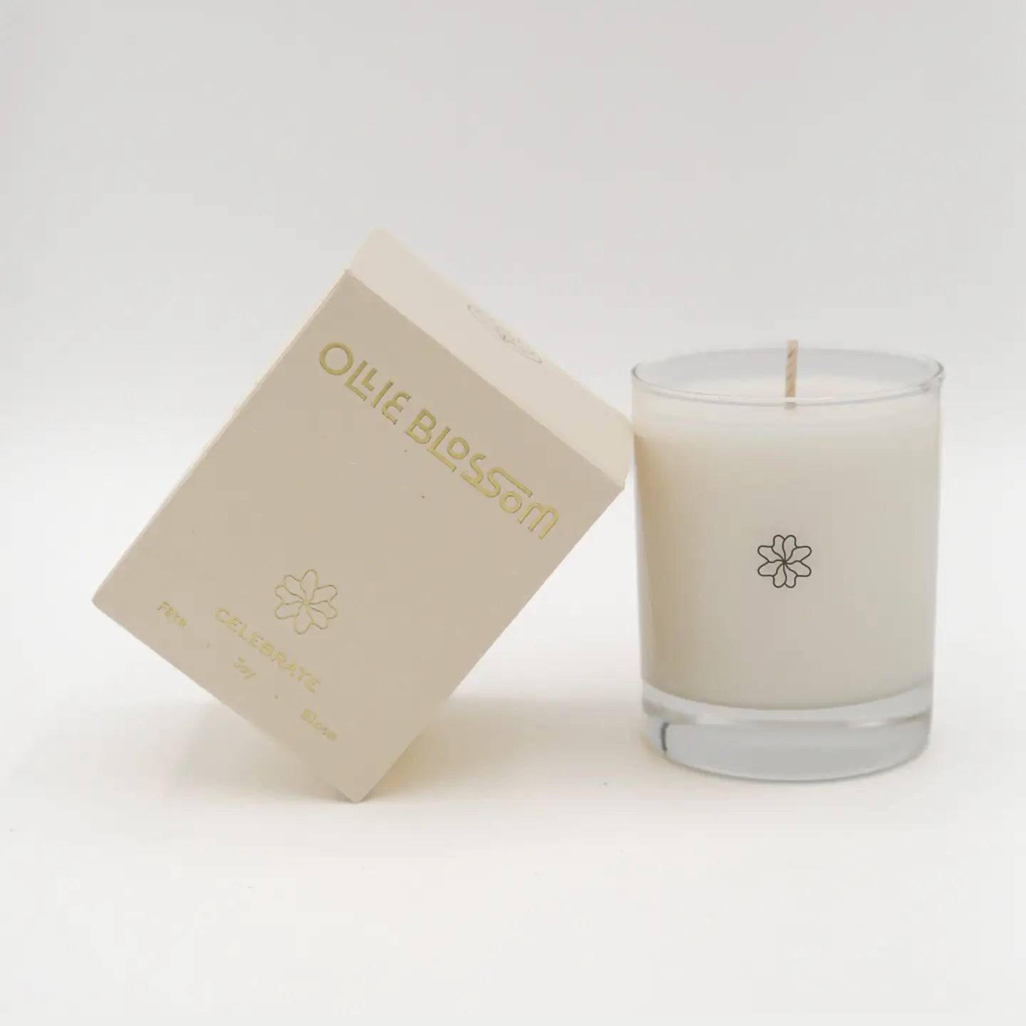 An oil-based candle in a clear glass jar next to its beige packaging box, both featuring the scent name 'Olive Blossom' in gold lettering.