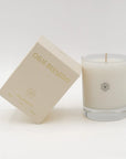 An oil-based candle in a clear glass jar next to its beige packaging box, both featuring the scent name 'Olive Blossom' in gold lettering.