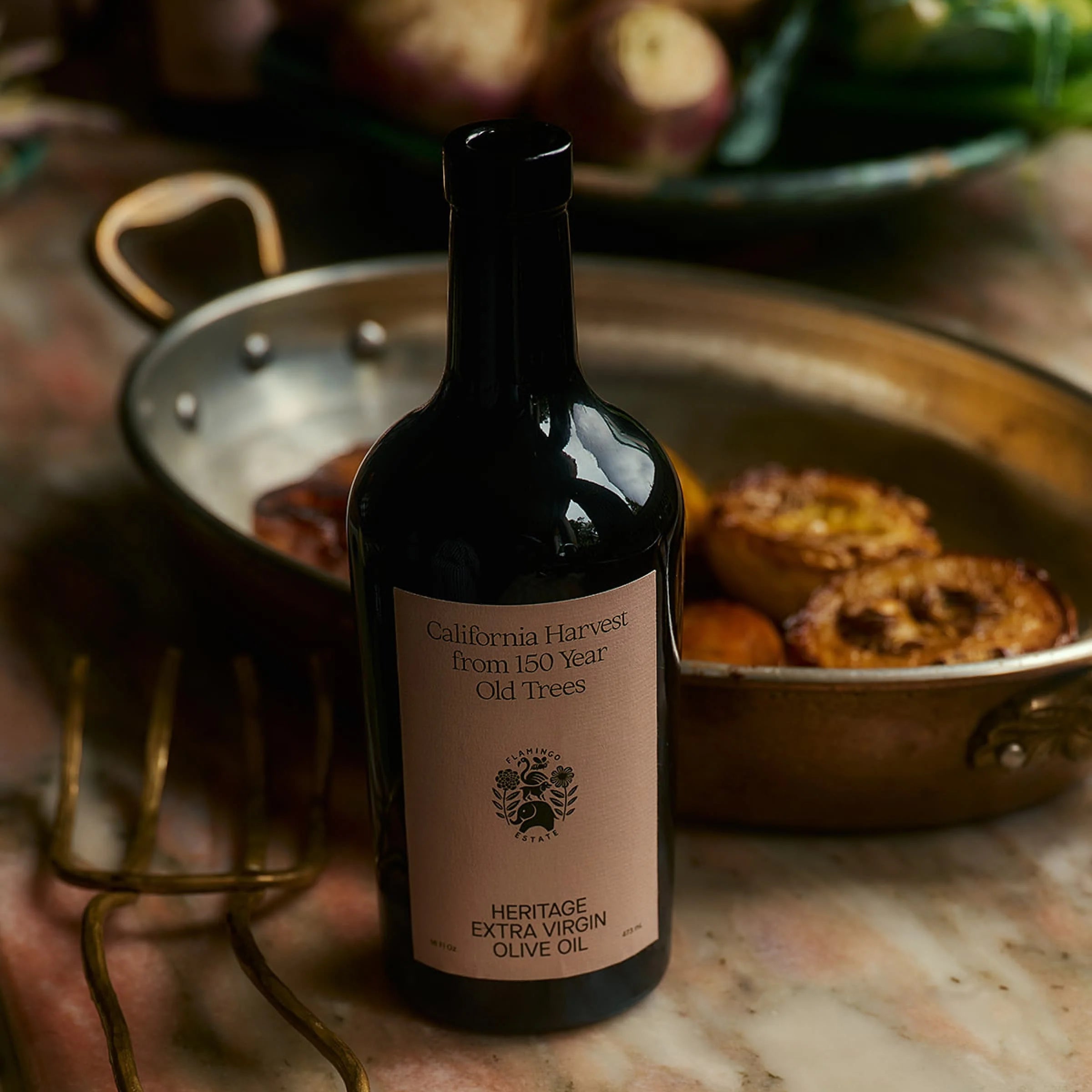 Bottle of California Harvest olive oil on a marble surface with a pan of food in the background