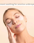 Woman applying eye patches with text 'Instant soothing for sensitive undereyes' on a beige background