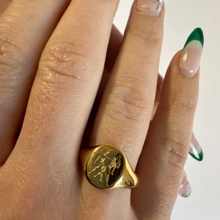 A woman&#39;s hand wearing a gold plated ring with a taurus zodiac symbol engraved into the ring.