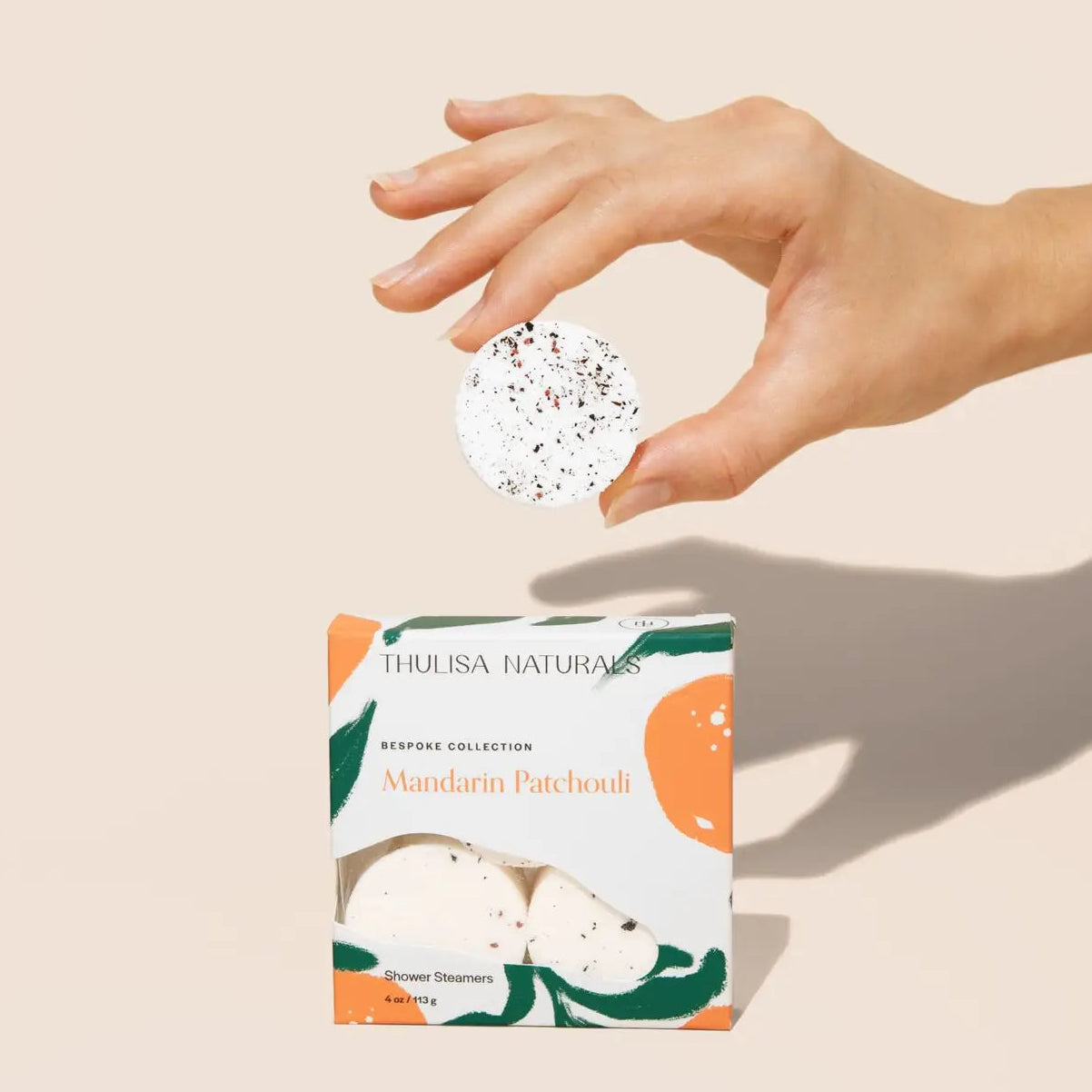 Hand holding a Thulisa Naturals product with packaging in the foreground on a beige background