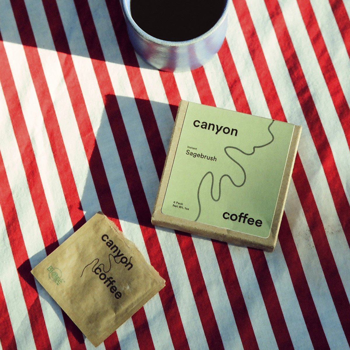 sage green instant coffee box on red &amp; white striped tablecloth with a mug of coffee next to it